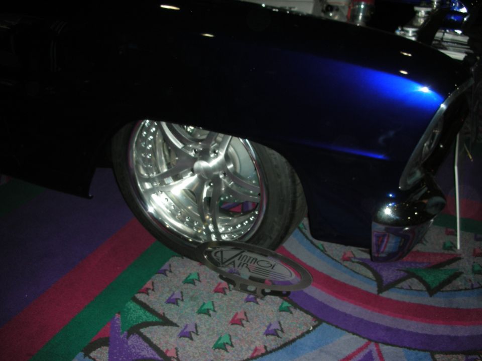Car fender, large chrome wheel, and a removed hubcap with 'VINTAGE AIR' text. The car is dark blue