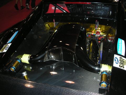 1998 Ford Crown Victoria - The engine bay of a race car features exposed carbon fiber components and gold-colored heat shielding.