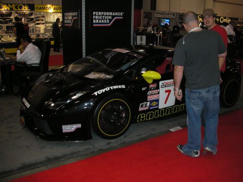 1998 Ford Crown Victoria - A black sports car with racing decals is displayed indoors, with two men standing nearby.