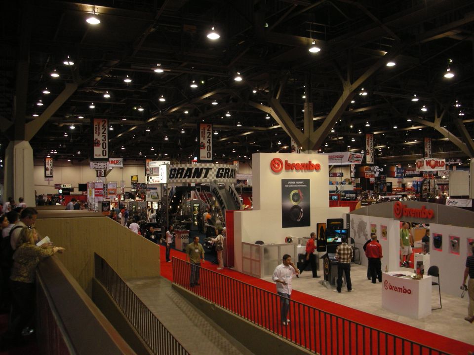 Interior view of a large convention hall with multiple vendor booths, including Brembo and Grant. People are walking around