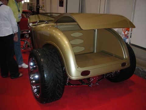 1998 Ford Crown Victoria - A custom hot rod with a gold finish and oversized rear tires is displayed on a red carpet.