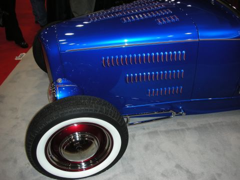 1998 Ford Crown Victoria - A bright blue hot rod is displayed with its front fender and wheel visible, classic white wall tires and red rim accents.