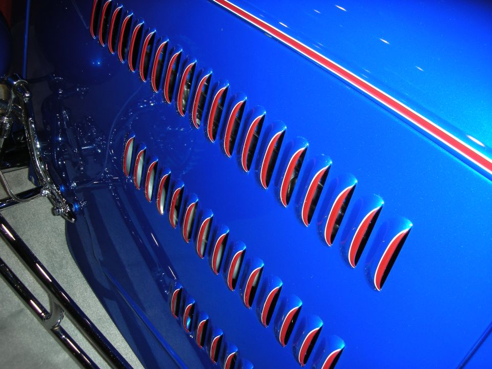 Close-up of a blue car fender with multiple red-lined vents and a red and white stripe