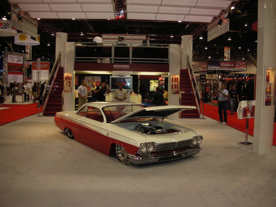 Two-tone red and white classic car with hood open showing engine at a show