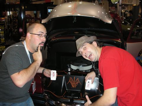 1998 Ford Crown Victoria - Two men playfully pose with their phones in front of a car's engine bay, decorated with custom pinstriping.