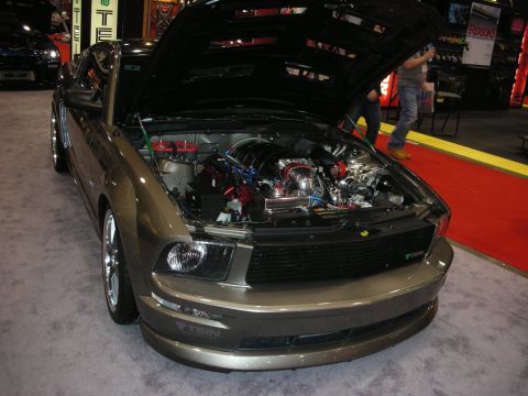 1998 Ford Crown Victoria - Customized 2005 Ford Mustang on display, engine exposed. A second vehicle is partially visible in the background.
