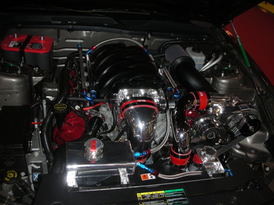 Engine bay with custom intake, chrome parts, and red accents. Looks like a V8