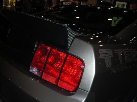 1998 Ford Crown Victoria - Close-up of a car's rear, showing a carbon fiber spoiler and distinctive triple-bar taillight, with "TEIN For Your Driving Pleasure" graphi…