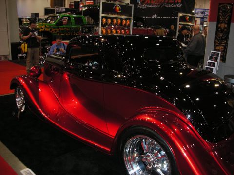 1998 Ford Crown Victoria - A two-tone red and black custom coupe is displayed indoors, with a green pickup truck visible behind it.
