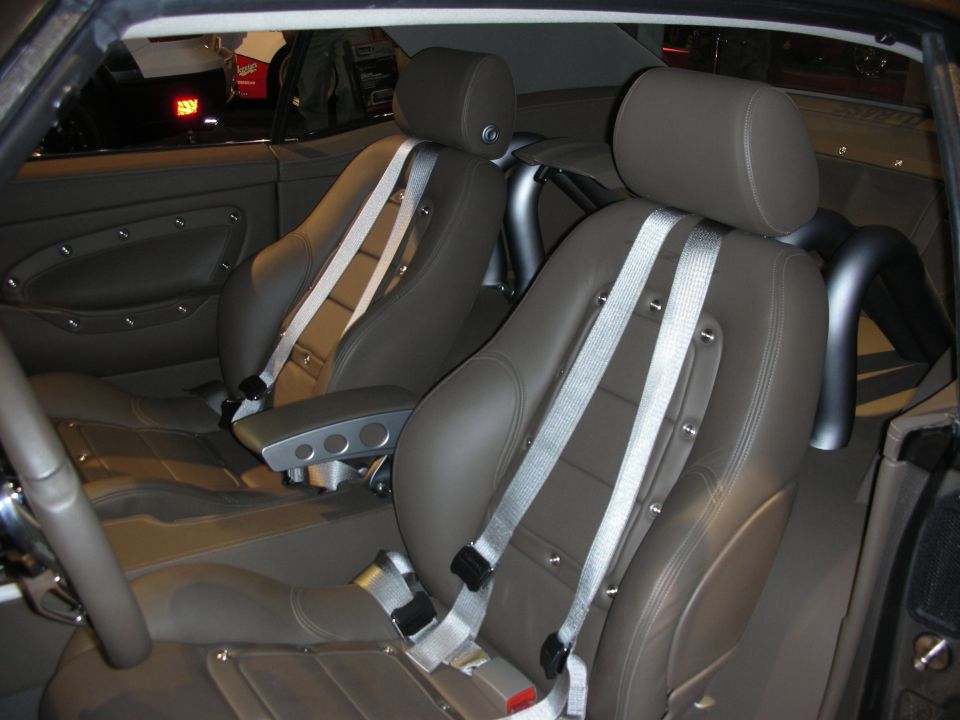 Car interior with two brown bucket seats, silver racing harnesses, and a roll bar