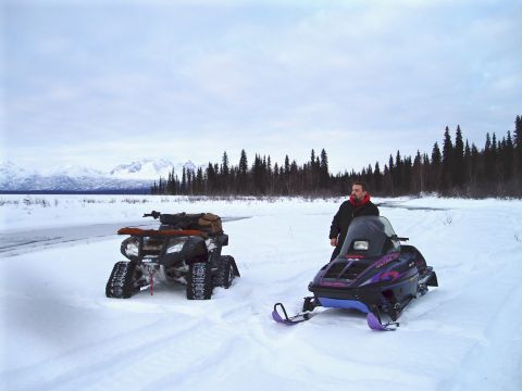 2000 Ford E350 - A man stands next to a snowmobile with an ATV parked nearby in a vast, snow-covered wilderness.