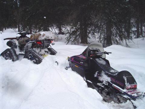 2000 Ford E350 - Two snowmobiles and an ATV are partially buried in snow in a wooded area.