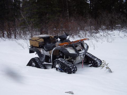 2000 Ford E350 - An all-terrain vehicle equipped with tracks is partially buried in snow, with cargo and a snowboard attached.