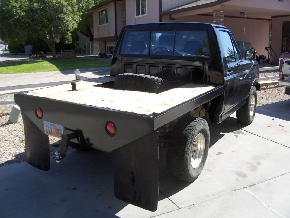 Black flatbed truck with a wooden bed, dual rear wheels, and a spare tire visible