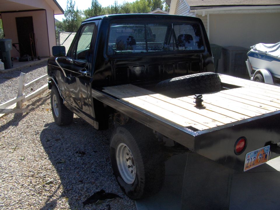 Black flatbed truck with wooden bed, spare tire visible