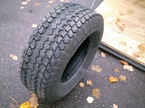 2001 Dodge 2500 - A single tire rests on a wet asphalt surface, surrounded by scattered autumn leaves.