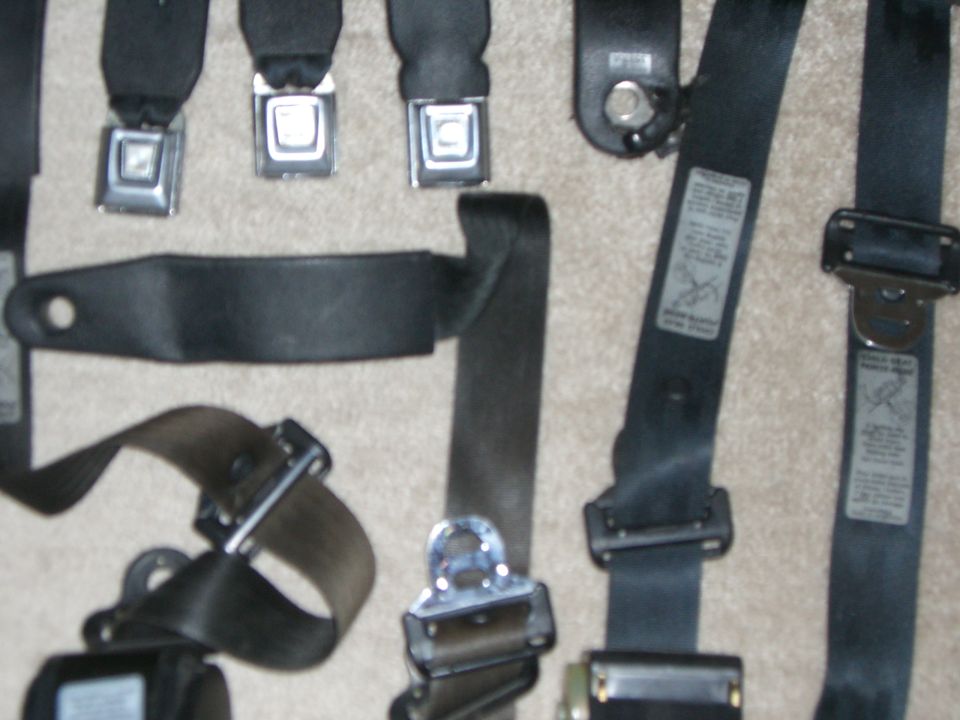 Several black seat belts with metal buckles and fabric straps are laid out on a carpeted surface
