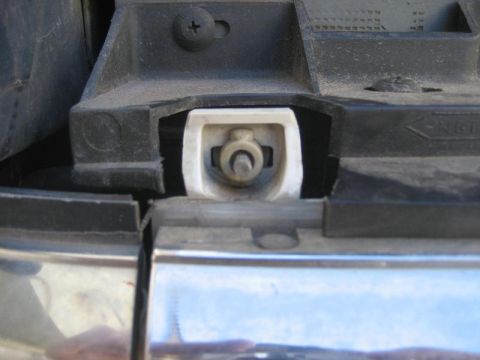 1987 Ford Bronco - Close-up view of a headlight mounting bracket assembly, showing the clip mechanism and surrounding plastic and chrome trim.