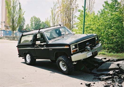 1985 Ford Bronco with roof rack driving over a hole in the road