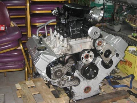 2007 Ford Mustang - A V8 engine with a supercharger is displayed on wooden pallets, with chairs and shelving in the background.