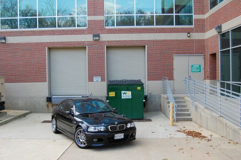 2002 BMW M3 - A black 2002 BMW M3 is parked in front of a brick building with loading docks.