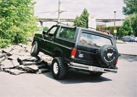 1985 Ford Bronco - Black Ford Bronco with white wheels navigates a pile of broken asphalt.