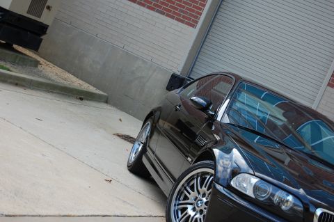 2002 BMW M3 - A black BMW M3 is parked in front of a brick building with a closed garage door.