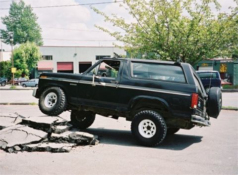 1985 Ford Bronco - Black 1985 Ford Bronco navigates a broken section of road, its off-road capabilities.