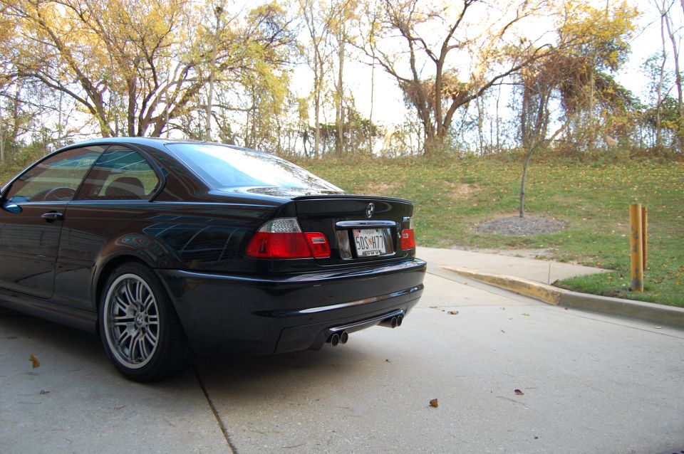 Black coupe with a rear spoiler and quad exhaust pipes, parked on concrete