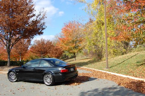 2002 BMW M3 - A black BMW M3 is parked on the side of the road during autumn, with colorful leaves scattered around.