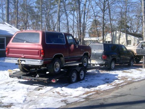 1986 Chevrolet C/K Pickup - Red SUV being transported on a trailer, with other vehicles visible in the background.
