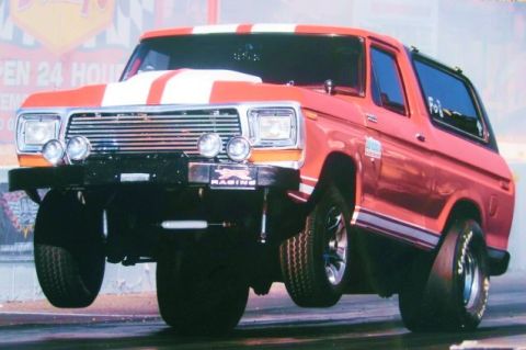 1979 Ford Bronco - This modified 1978 Ford Bronco is captured mid-air during a drag race, its racing stripes and lifted front wheels.