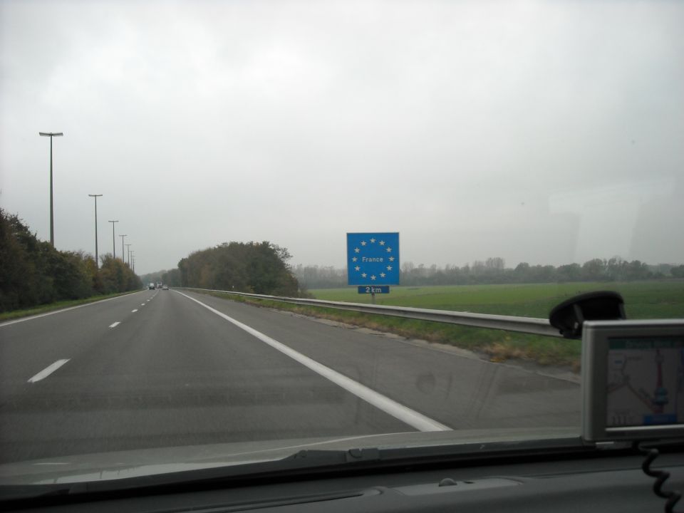Highway view approaching a sign indicating France is 2 km away, with a GPS device visible on the dashboard
