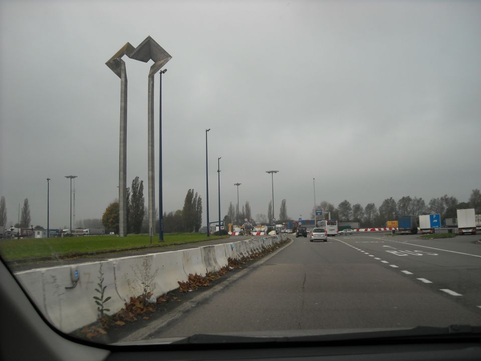 Roadside scene with concrete barriers, trucks, and cars under a cloudy sky