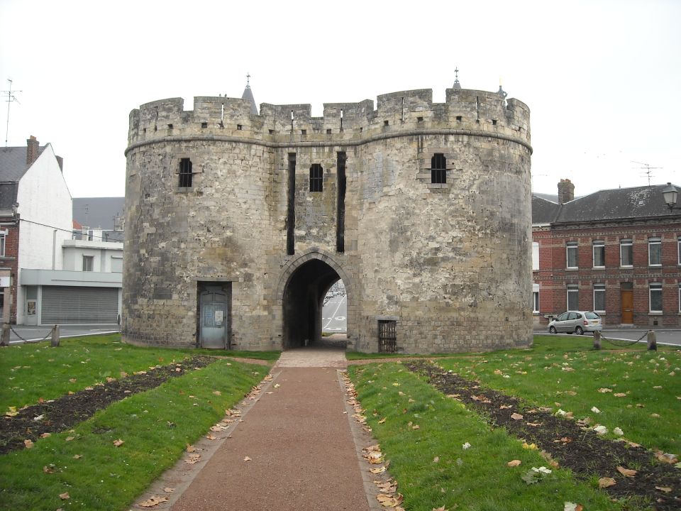 Stone gatehouse with crenellations and arched entryway, a silver car parked nearby