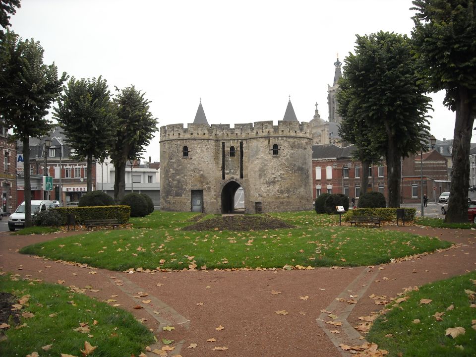 Stone gatehouse with twin turrets and arched entryway, surrounded by a park with trees and fallen leaves