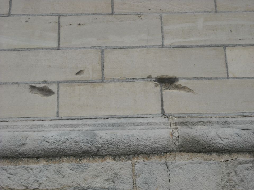 Close-up of a stone wall showing damage to several blocks and a decorative stone trim
