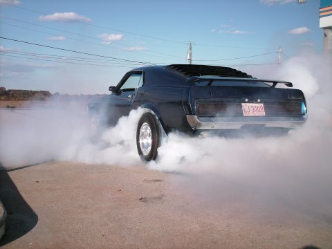 1970 Ford Mustang - A dark blue 1970 Ford Mustang performs a burnout, kicking up a large cloud of smoke. The rear view shows the license plate LJ-3408.