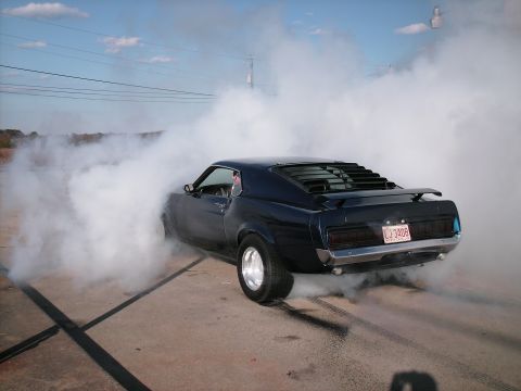 1970 Ford Mustang - A classic Mustang performs a burnout, filling the air with smoke and leaving tire marks on the pavement.