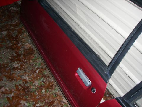 1988 Ford Bronco - A detached car door rests on the ground next to a building, showing its exterior and door handle.