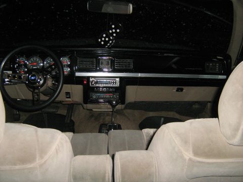 1988 Mercury Grand Marquis - The interior of a car features an aftermarket steering wheel, radio, and fuzzy dice hanging from the rearview mirror.