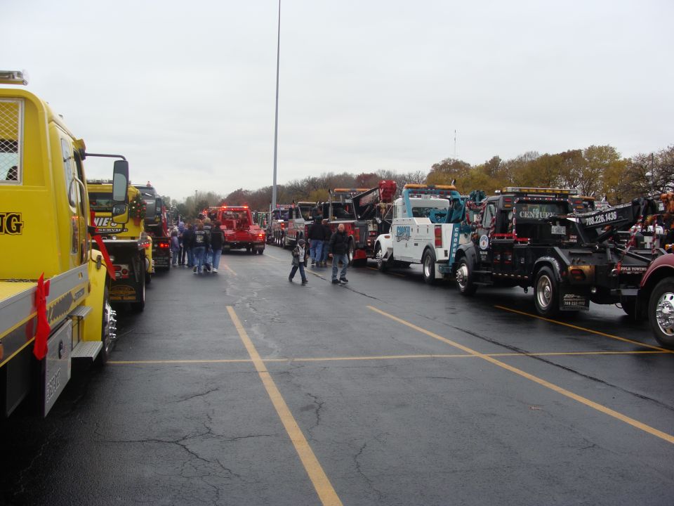 Multiple tow trucks parked in a lot with people standing around