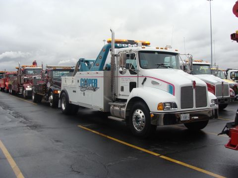 1992 Ford Bronco - A line of tow trucks are parked in a lot under an overcast sky.