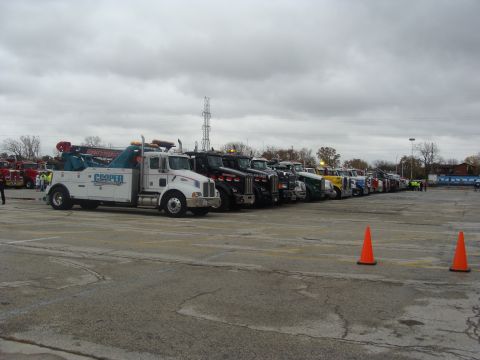 1992 Ford Bronco - Multiple tow trucks and semi-trucks are parked in a line in an outdoor lot.
