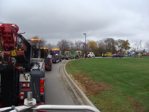 1992 Ford Bronco - A convoy of tow trucks is lined up on a road next to a grassy area under an overcast sky.