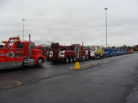 1992 Ford Bronco - Multiple tow trucks are lined up in a parking lot on an overcast day.