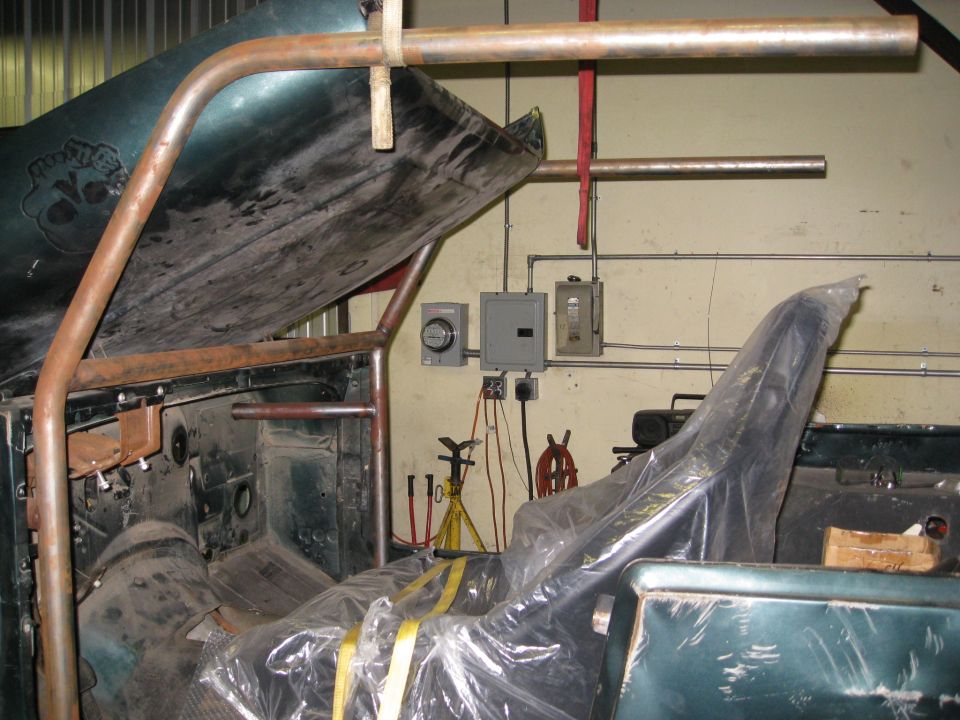 Green Jeep interior under construction with roll cage, plastic-wrapped seats, and electrical panels on wall