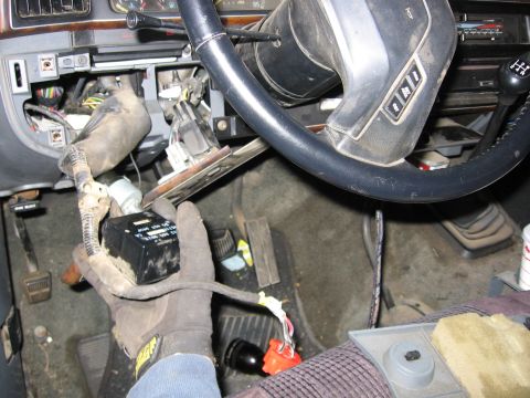 1989 Ford Bronco - A close-up shot of a vehicle's interior reveals exposed wiring and a hand holding a black electronic module near the steering column.
