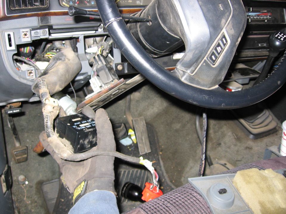 Interior view of a vehicle's dashboard with exposed wiring and a hand holding a black module
