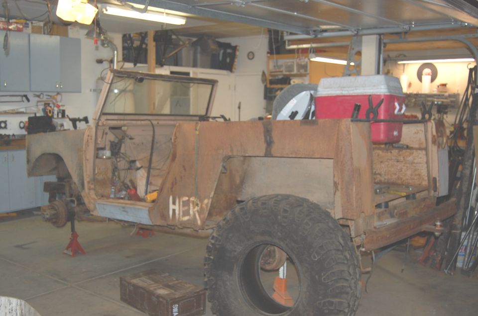 Rusty doorless Scout on jack stands, rear fenders cut away, loose mud tire at the rear